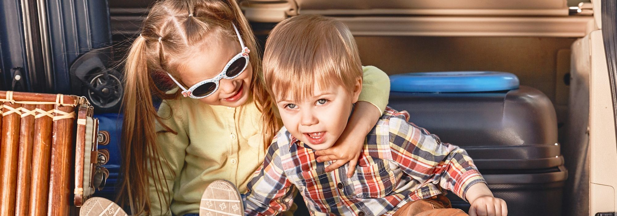 Beginning of the trip. Little cute kids in the trunk of a car with suitcases. Family road trip