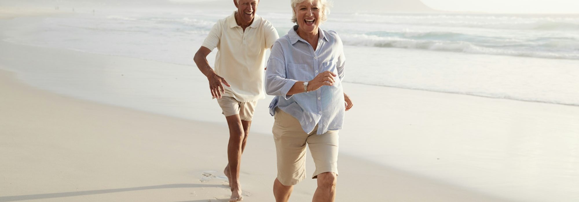 Senior Retired Couple Running Along Summer Beach Together